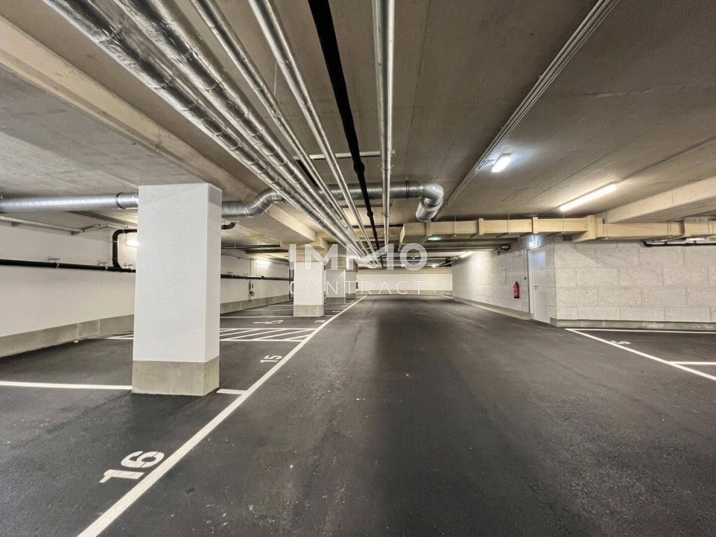 Geräumige Tiefgarage mit markierten Parkplätzen, Säulen und sichtbaren Versorgungsleitungen an der Decke.