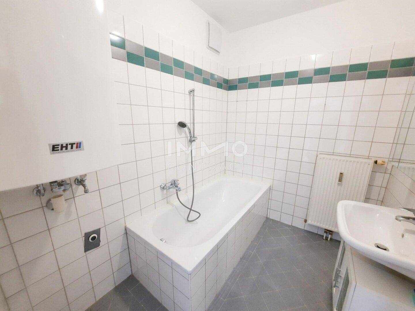 Badezimmer mit Badewanne, weißen Fliesen, farbiger Bordüre und Heizkörper.