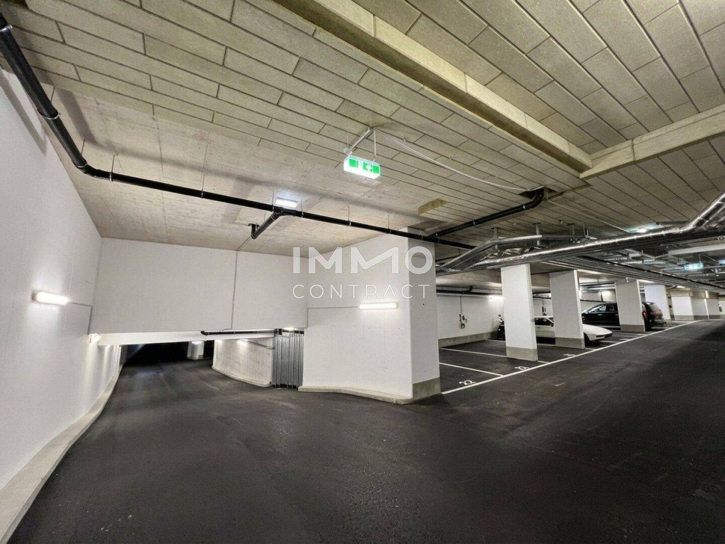 Moderne Tiefgarage mit breiter Zufahrtsrampe, klaren Markierungen und sichtbaren Installationen.