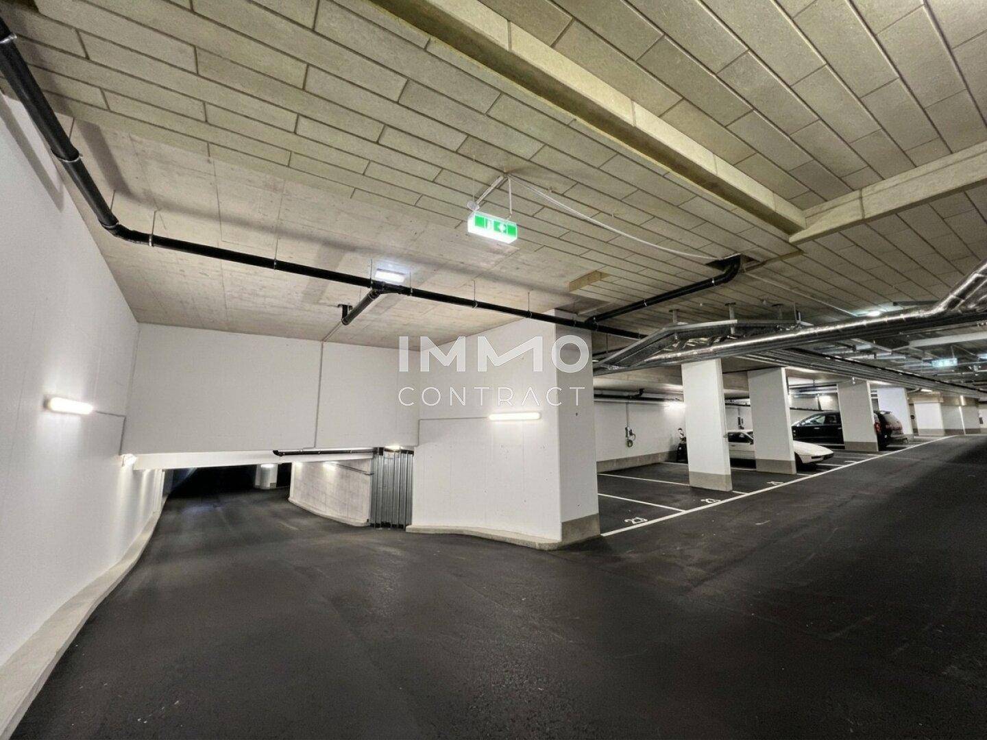 Einfahrt zur Tiefgarage mit hellen Wänden, Säulen und gut beleuchteten Parkbereichen.