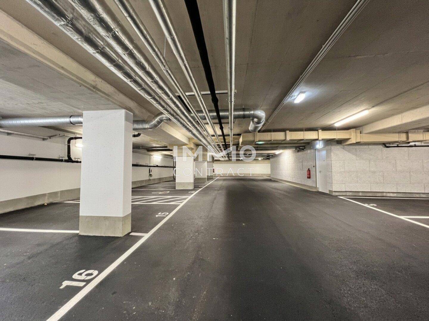 Geräumige Tiefgarage mit markierten Stellplätzen und sichtbaren Installationen an der Decke.