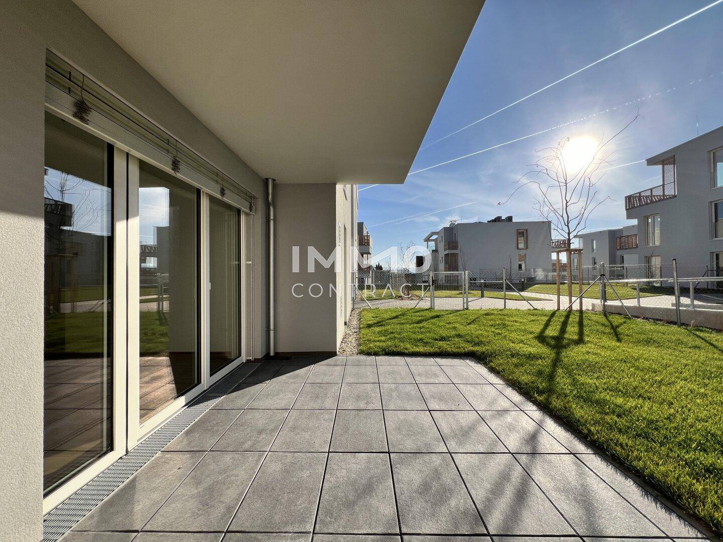 Geräumige Terrasse mit modernen Fliesen und angrenzender Rasenfläche unter strahlend blauem Himmel.