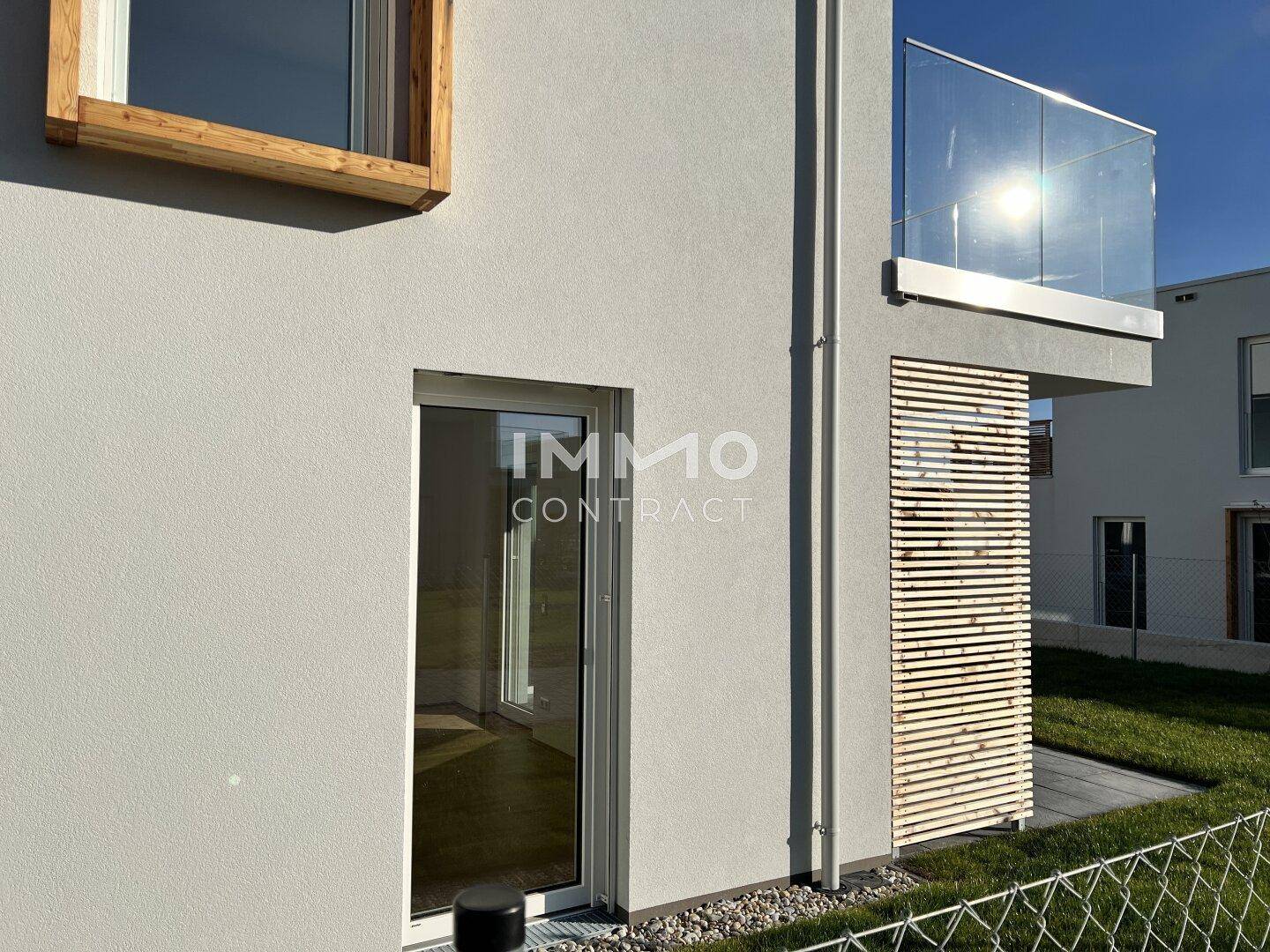 Moderne Fassade mit großen Fenstern und einem Balkon mit Glasgeländer.