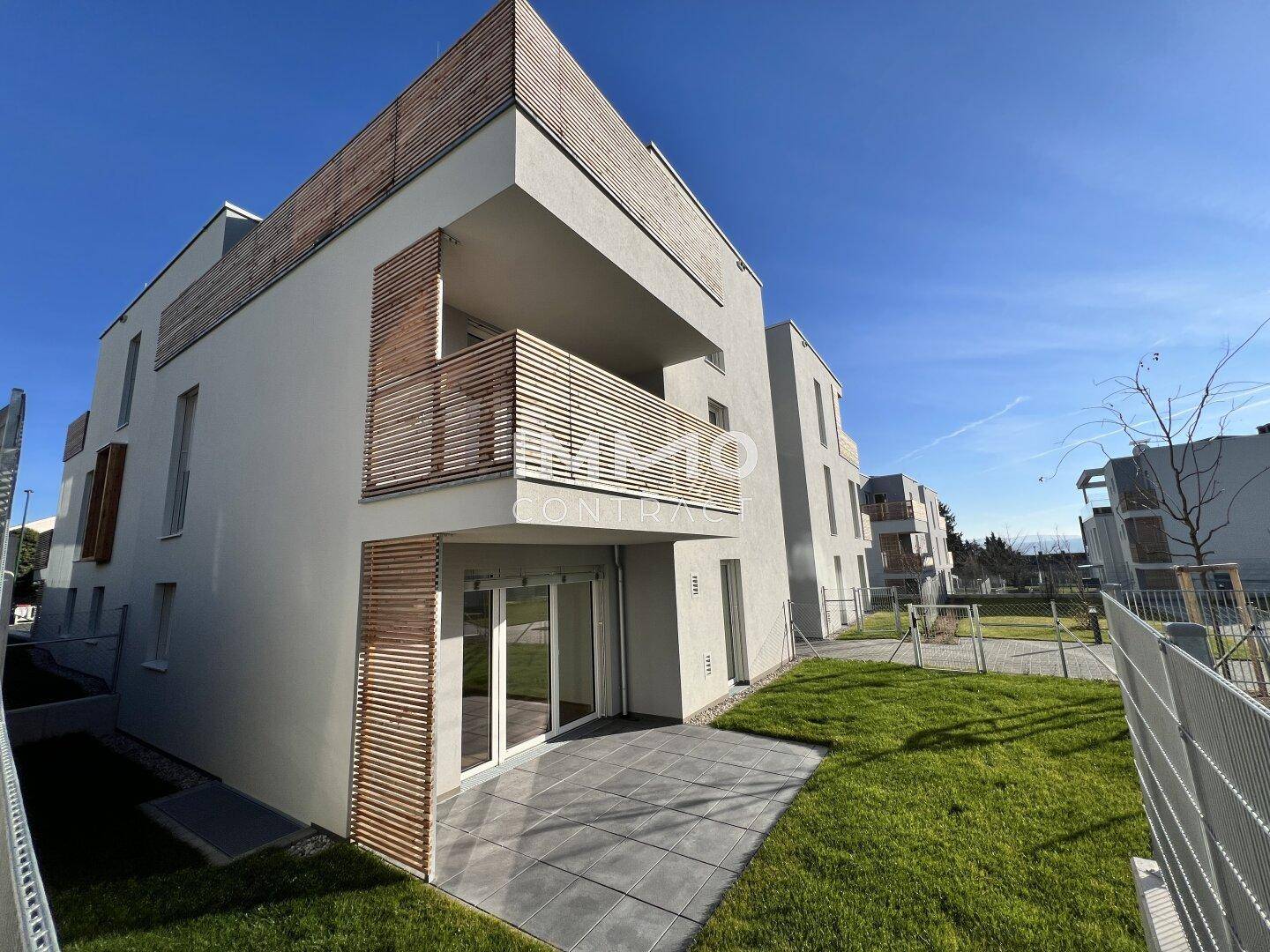 Modernes Mehrfamilienhaus mit hellgrauer Fassade und Holzdetails an den Balkonen.