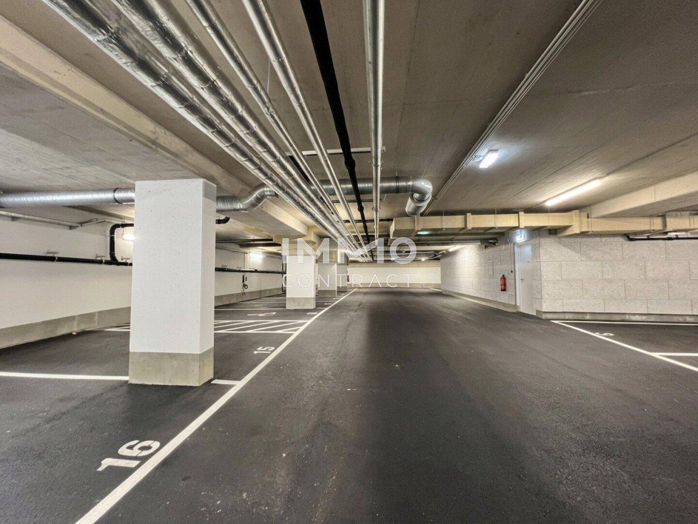 Geräumige Tiefgarage mit markierten Stellplätzen und sichtbaren Lüftungsrohren.