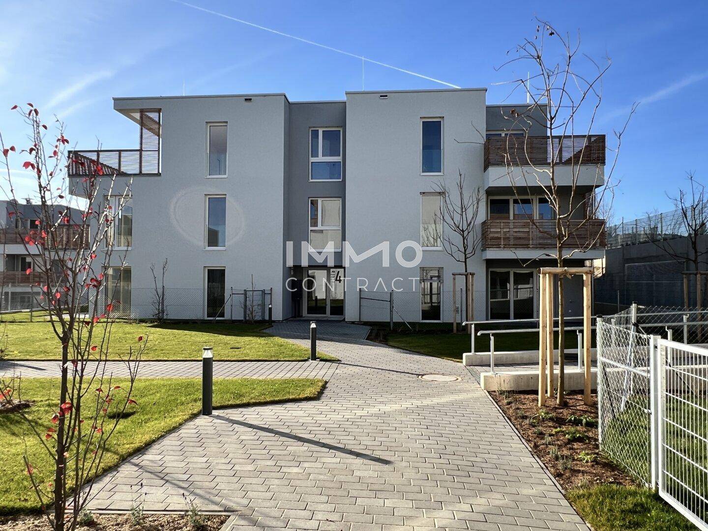 Modernes Wohngebäude mit gepflastertem Weg, Rasenflächen und jungen Bäumen im Vordergrund.