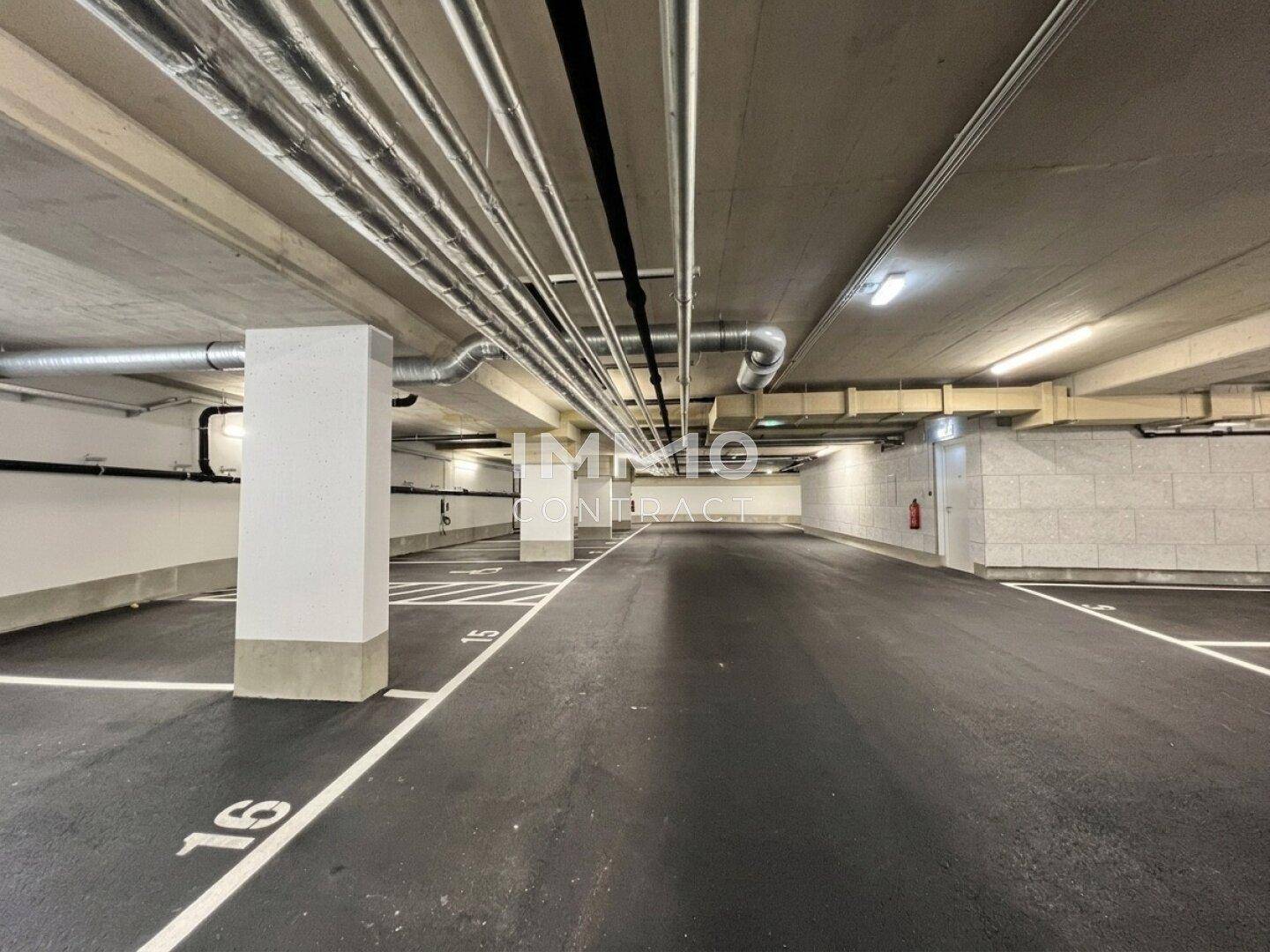 Geräumige Tiefgarage mit markierten Stellplätzen und sichtbaren Versorgungsleitungen an der Decke.