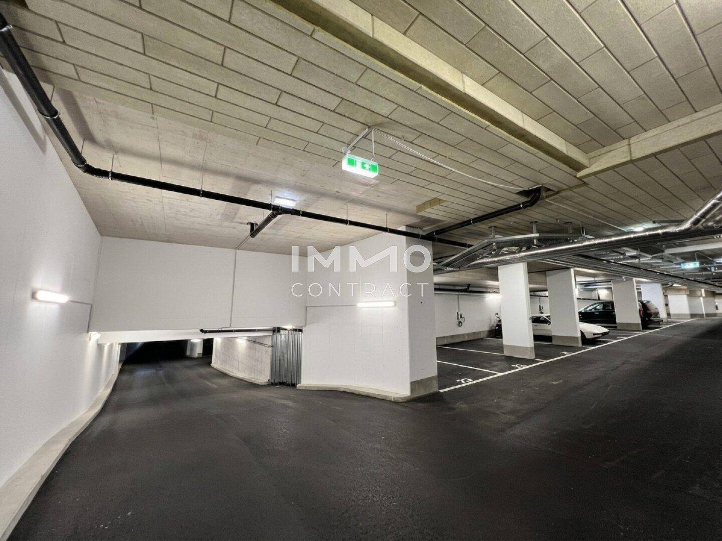 Einfahrt zu einer modernen Tiefgarage mit hellen Wänden und gut beleuchteten Stellplätzen.