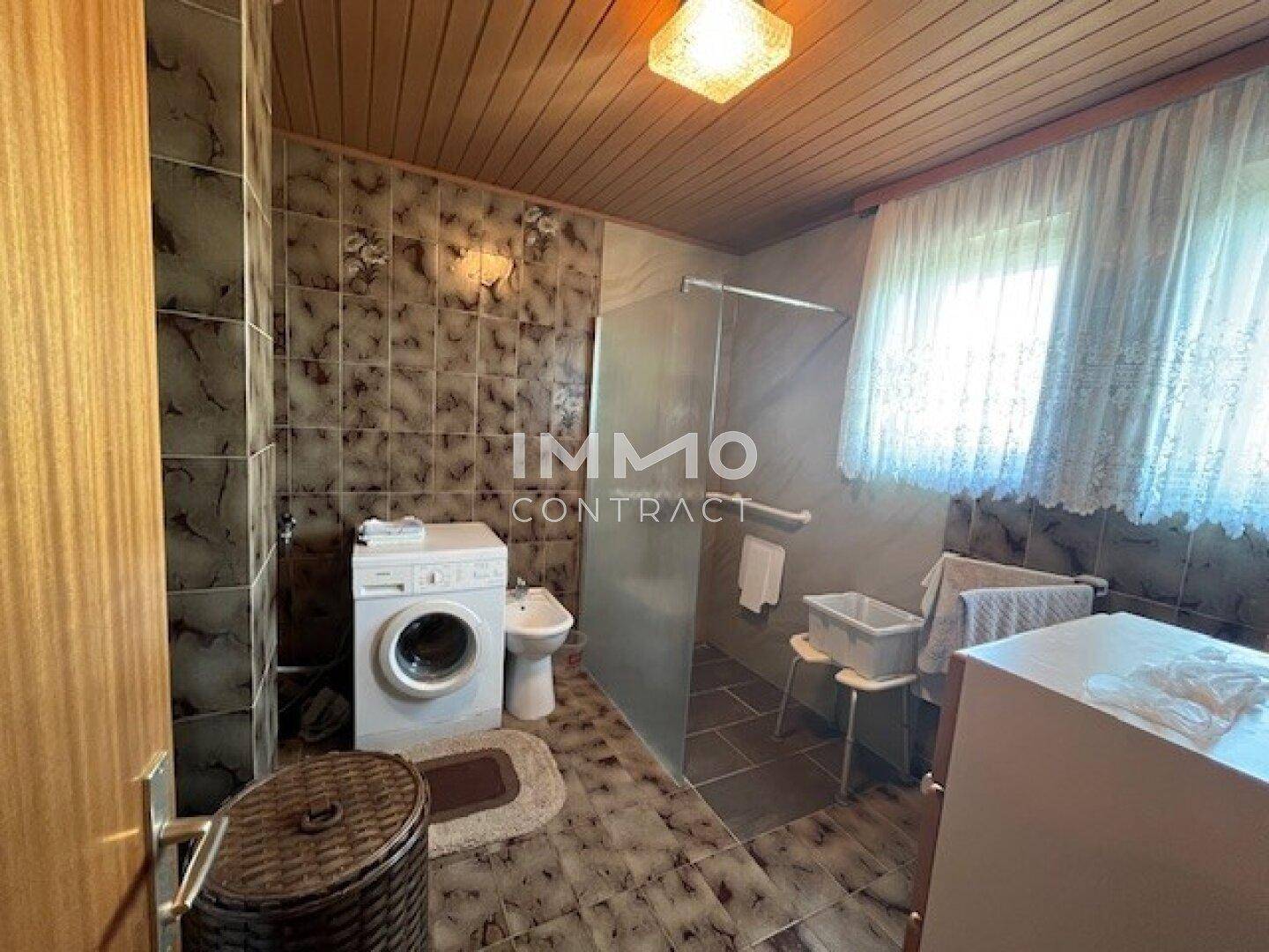 Badezimmer mit Waschmaschine, Bidet, Dusche und gemusterten Fliesen an Wänden und Boden.