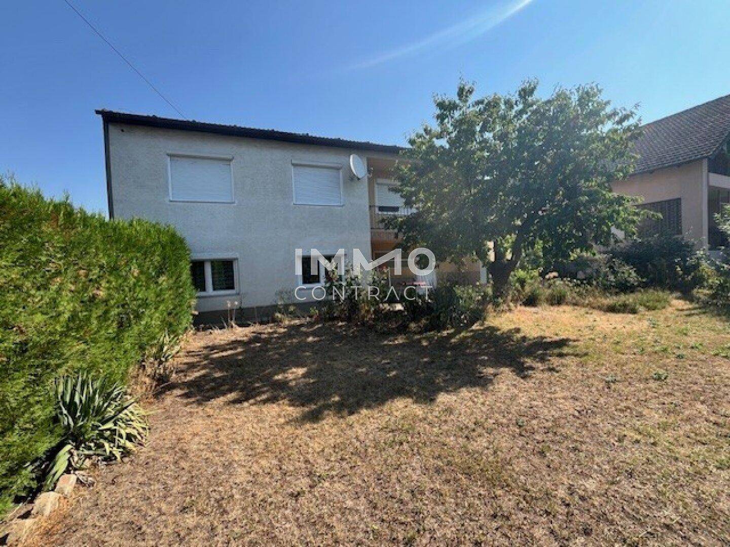 Rückansicht eines Wohnhauses mit einem Baum und einem ungepflegten Rasen im Gartenbereich.