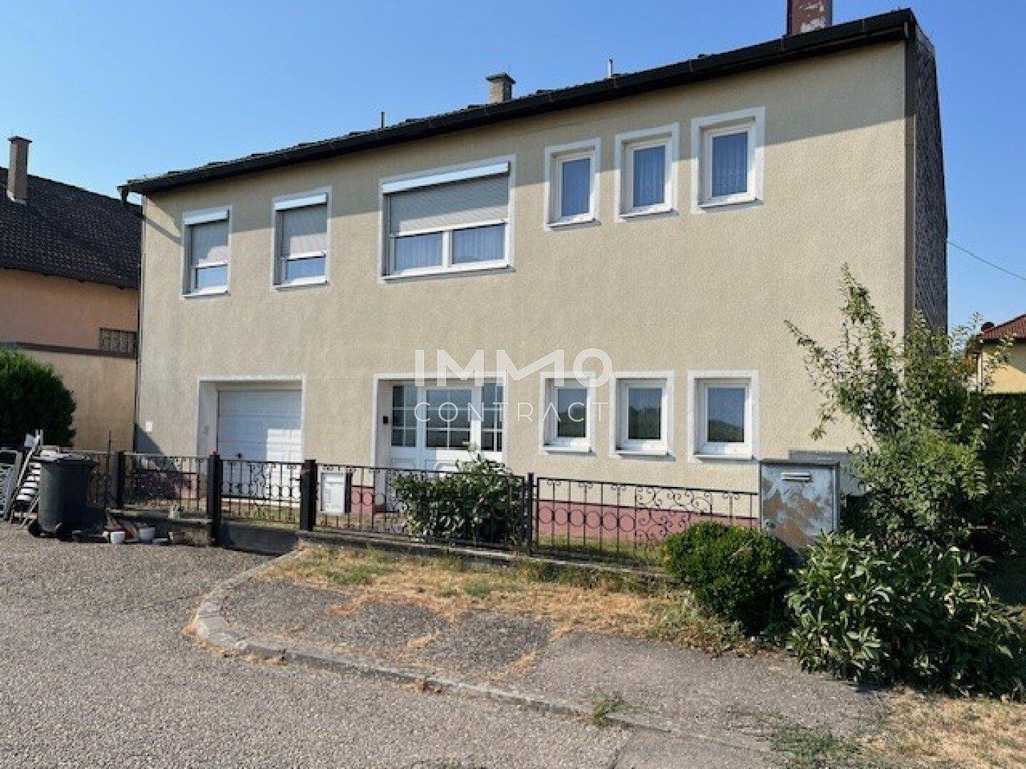 Vorderansicht eines Wohnhauses mit mehreren Fenstern, Rollläden und einer Garage im Erdgeschoss.