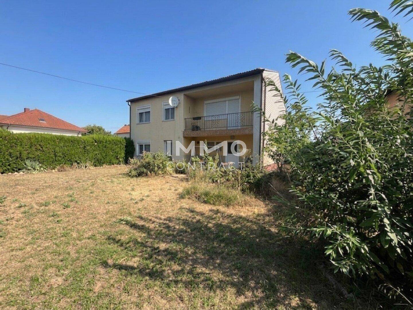 Rückansicht eines Wohnhauses mit einem Balkon und einem großen, ungepflegten Gartenbereich.