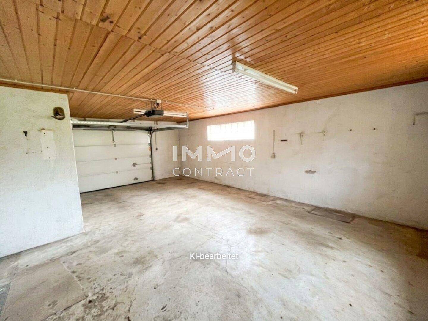 Geräumige Garage mit Betonboden, Holzdecke und einem großen Garagentor.