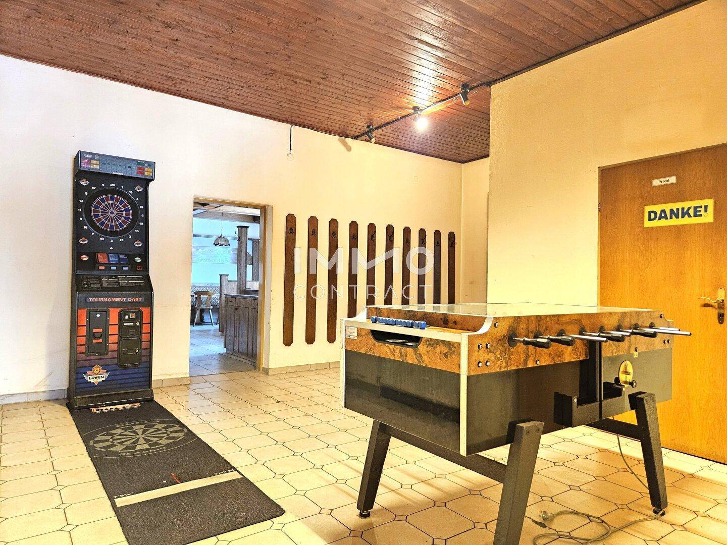 Spielzimmer mit Dartscheibe und Tischfußball, gefliestem Boden und Holzbalkendecke, ideal für Unterhaltung.