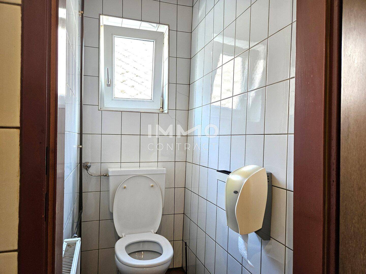 Damentoilette mit WC, Fenster und weißen Wandfliesen, bietet natürliche Belüftung und Helligkeit.