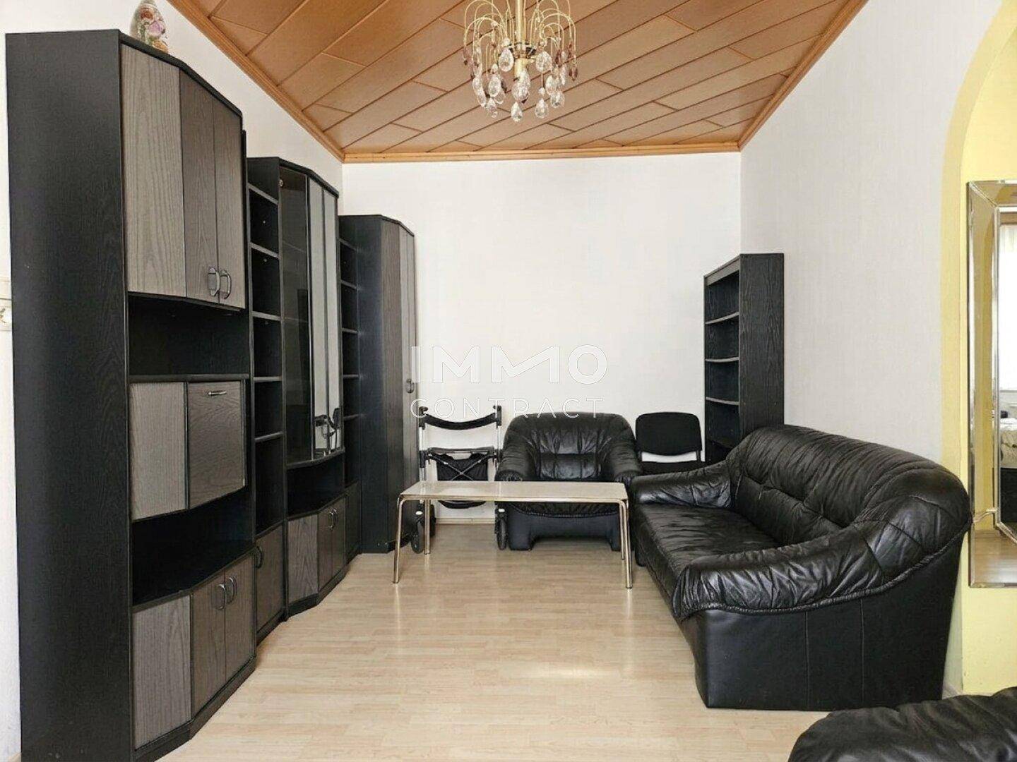 Wohnzimmer mit dunklen Ledermöbeln, Holzdecke und hellem Laminatboden, bietet eine gemütliche Atmosphäre.