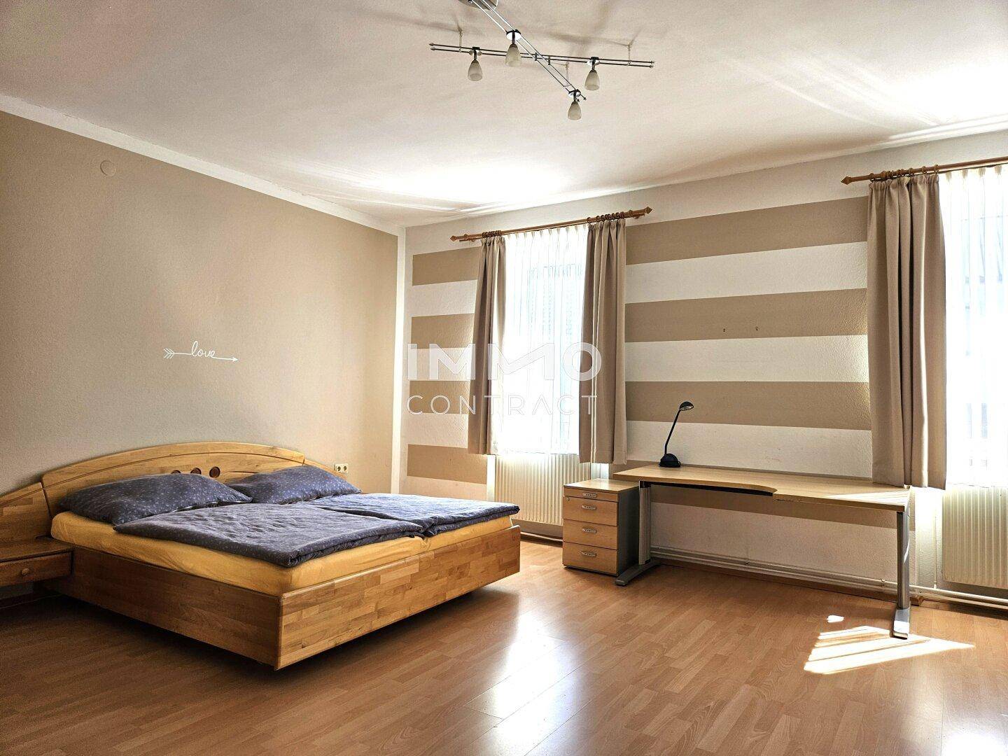 Geräumiges Schlafzimmer mit Doppelbett, Schreibtisch und großen Fenstern, bietet viel Tageslicht.