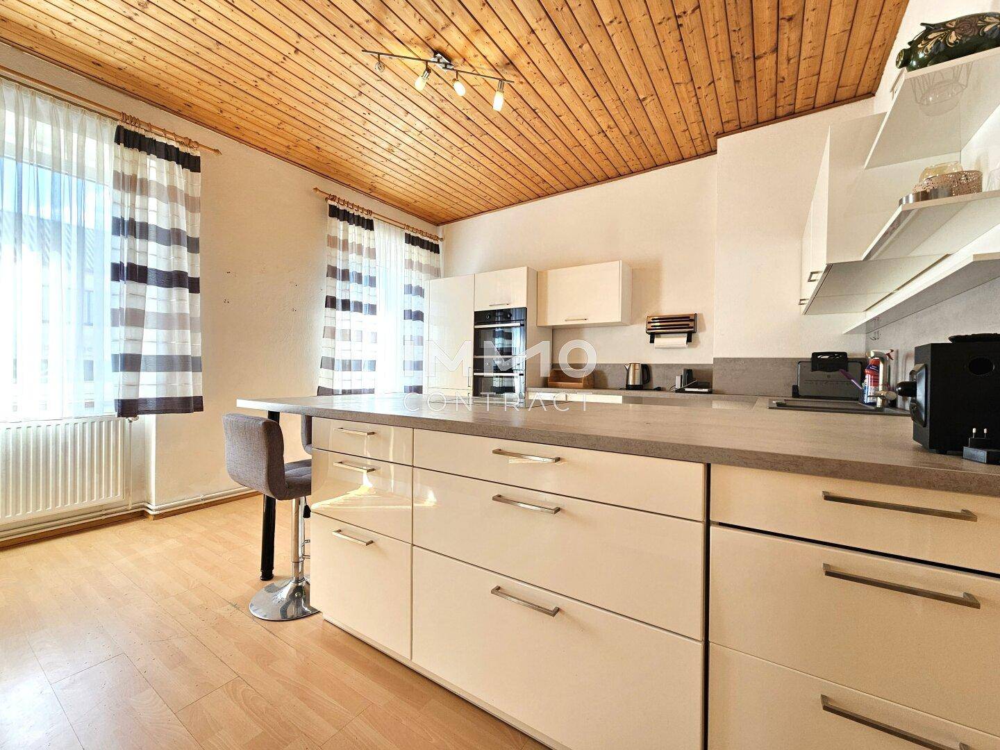 Helle Küche mit Kochinsel, großen Fenstern und Holzbalkendecke, bietet viel Arbeitsfläche und Stauraum.