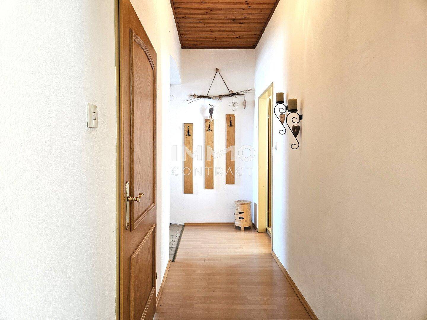 Heller Flur mit Holzboden und Holzdecke, führt zu weiteren Räumen und ist schlicht dekoriert.