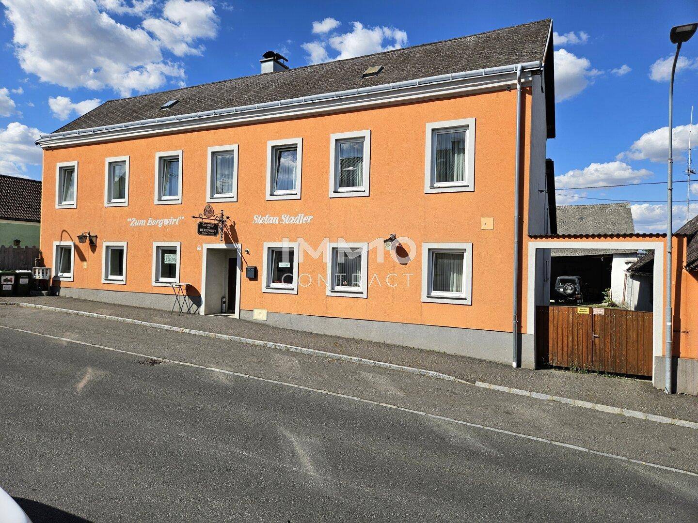 Traditionelles Gebäude mit orangefarbener Fassade, weißen Fenstern und einem Nebengebäude, an einer Straße gelegen.