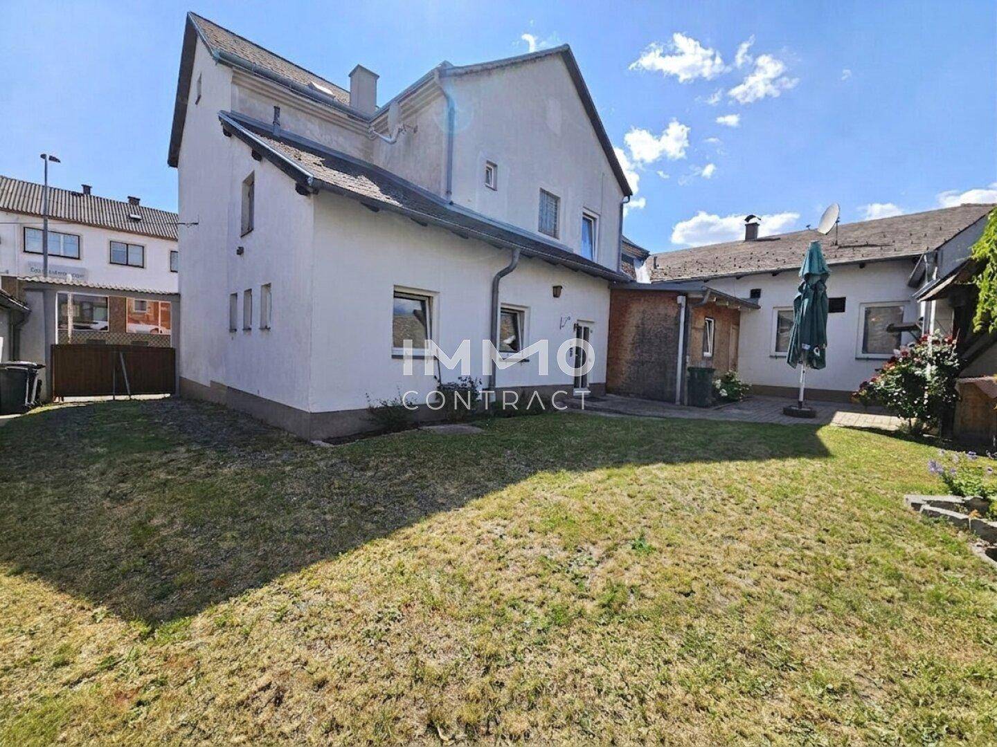 Hinteransicht eines weißen Hauses mit einem gepflegten Rasen und einem Sonnenschirm im Gartenbereich.