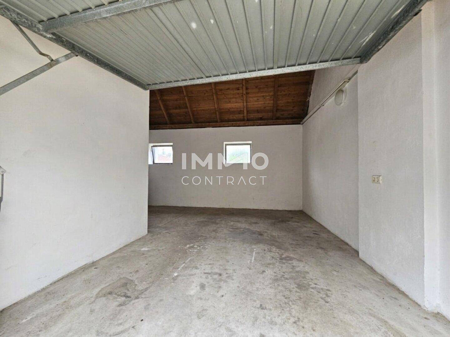 Leerer Raum mit weißen Wänden, Betonboden und einer Holzdecke mit sichtbaren Balken, ideal als Garage.