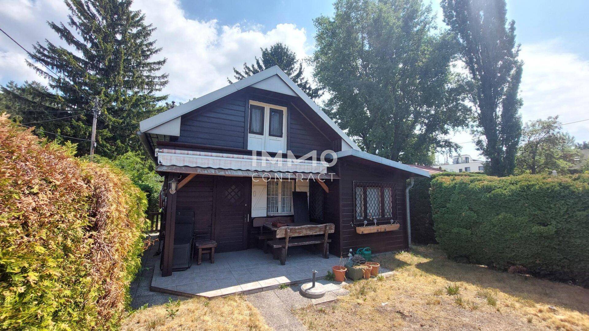 Rustikales Holzhaus mit Satteldach, umgeben von einem gepflegten Garten und hohen Bäumen.