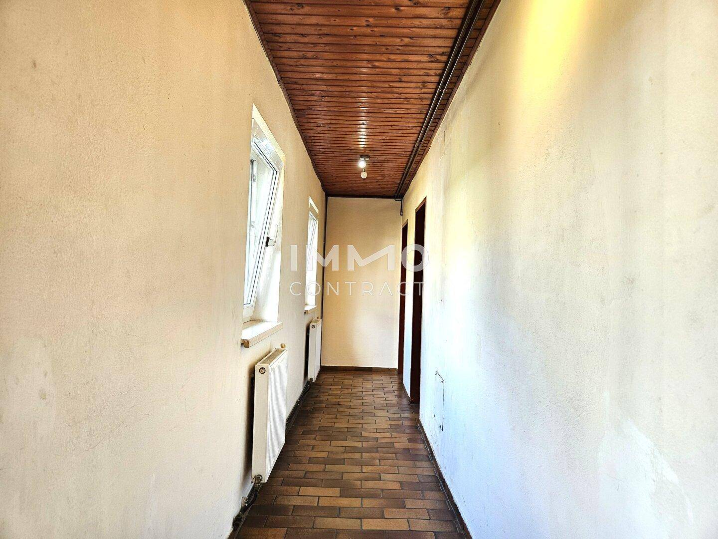 Heller Flur mit Fenstern, Heizkörpern und Holzbalkendecke, bietet Zugang zu verschiedenen Bereichen des Hauses.