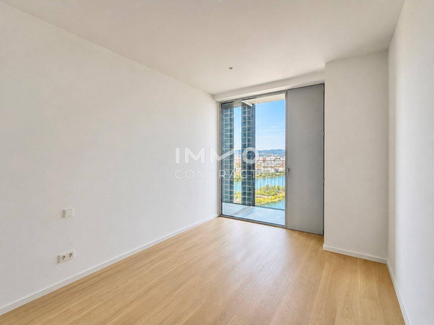 Helles Schlafzimmer mit Parkettboden und Zugang zu einem Balkon mit Stadtblick.
