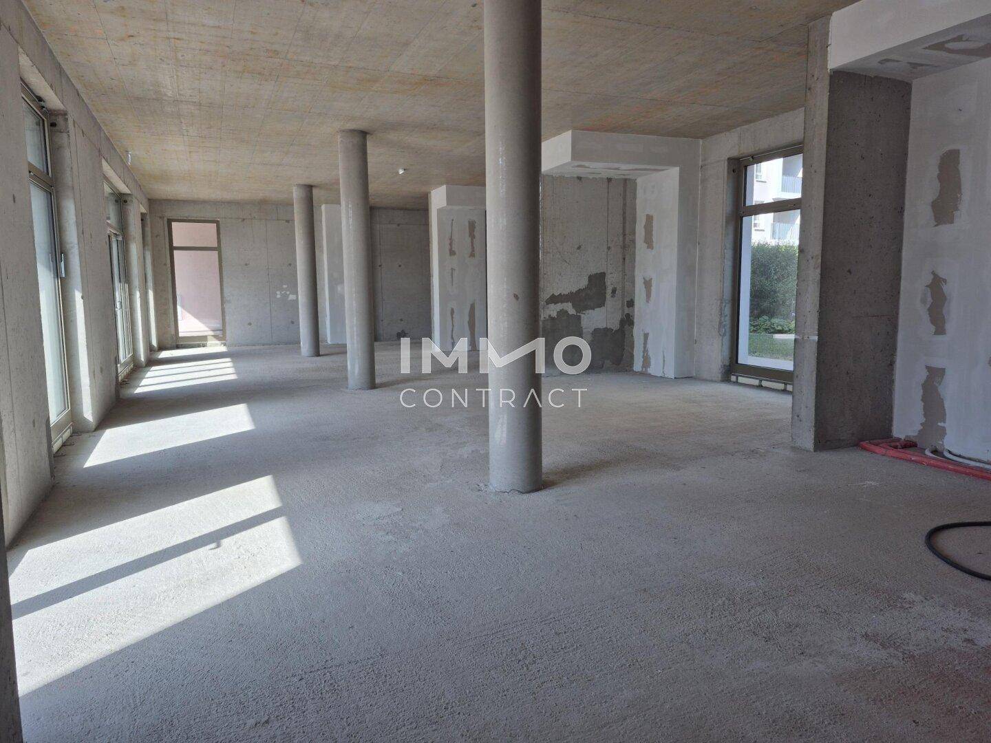 Großer, offener Gewerberaum im Rohbau mit Betonsäulen und -wänden, bereit für den Innenausbau.