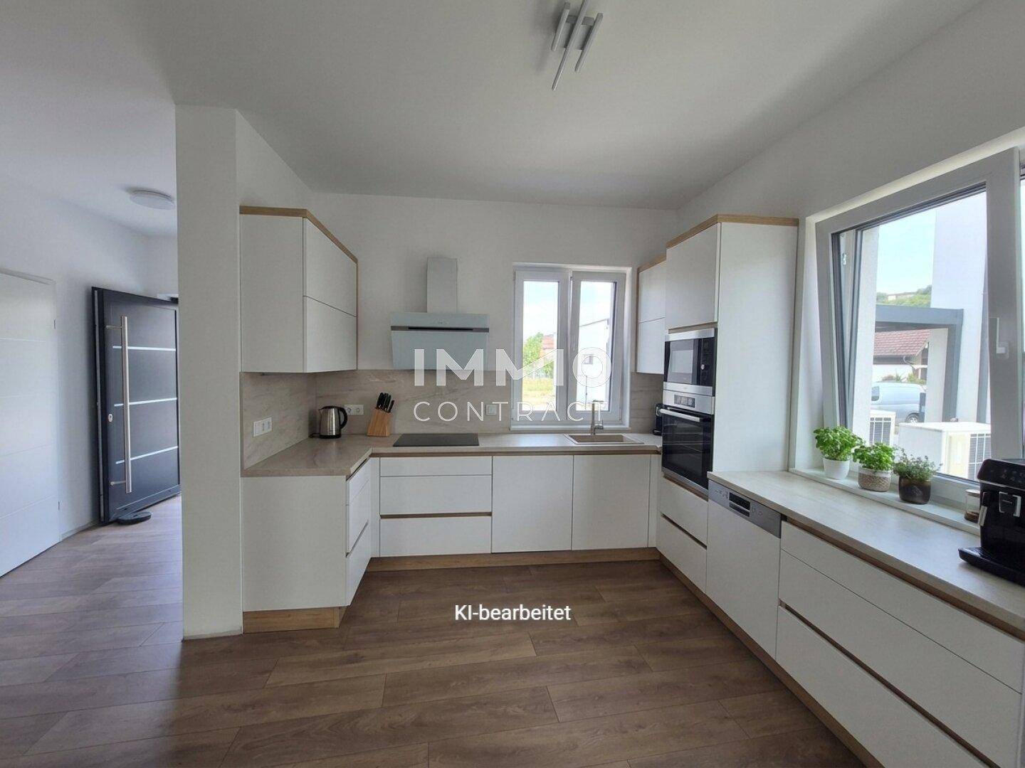 Helle, moderne Küche mit weißen Schränken, Holzoptik-Arbeitsplatten und großen Fenstern.