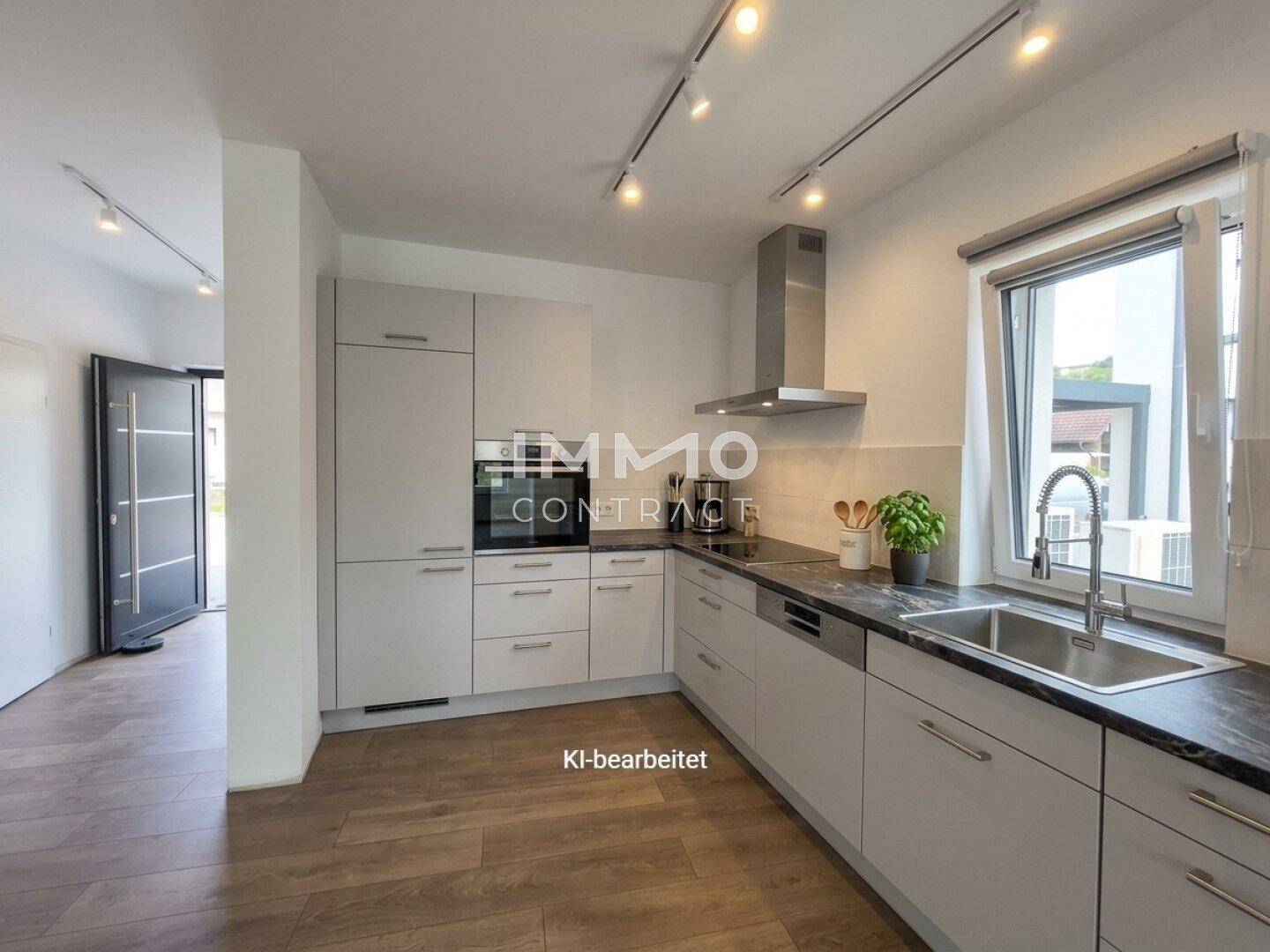 Moderne Küche mit hellgrauen Schränken, dunkler Arbeitsplatte und Fenster mit Blick nach draußen.