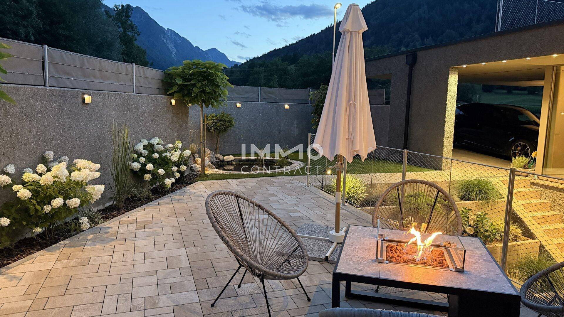 Gemütliche Terrasse am Abend mit Sitzgelegenheiten, Feuerstelle und Blick auf die umliegenden Berge.