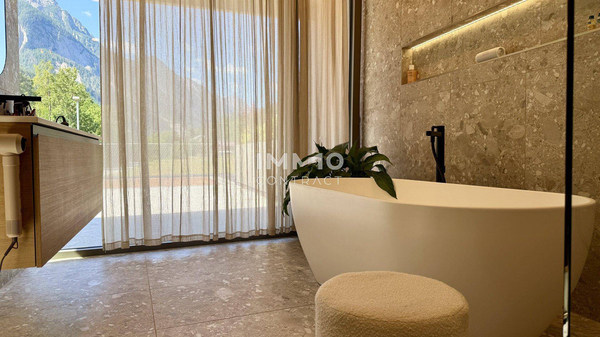 Modernes Badezimmer mit freistehender Badewanne, großen Fenstern und beeindruckendem Bergblick.