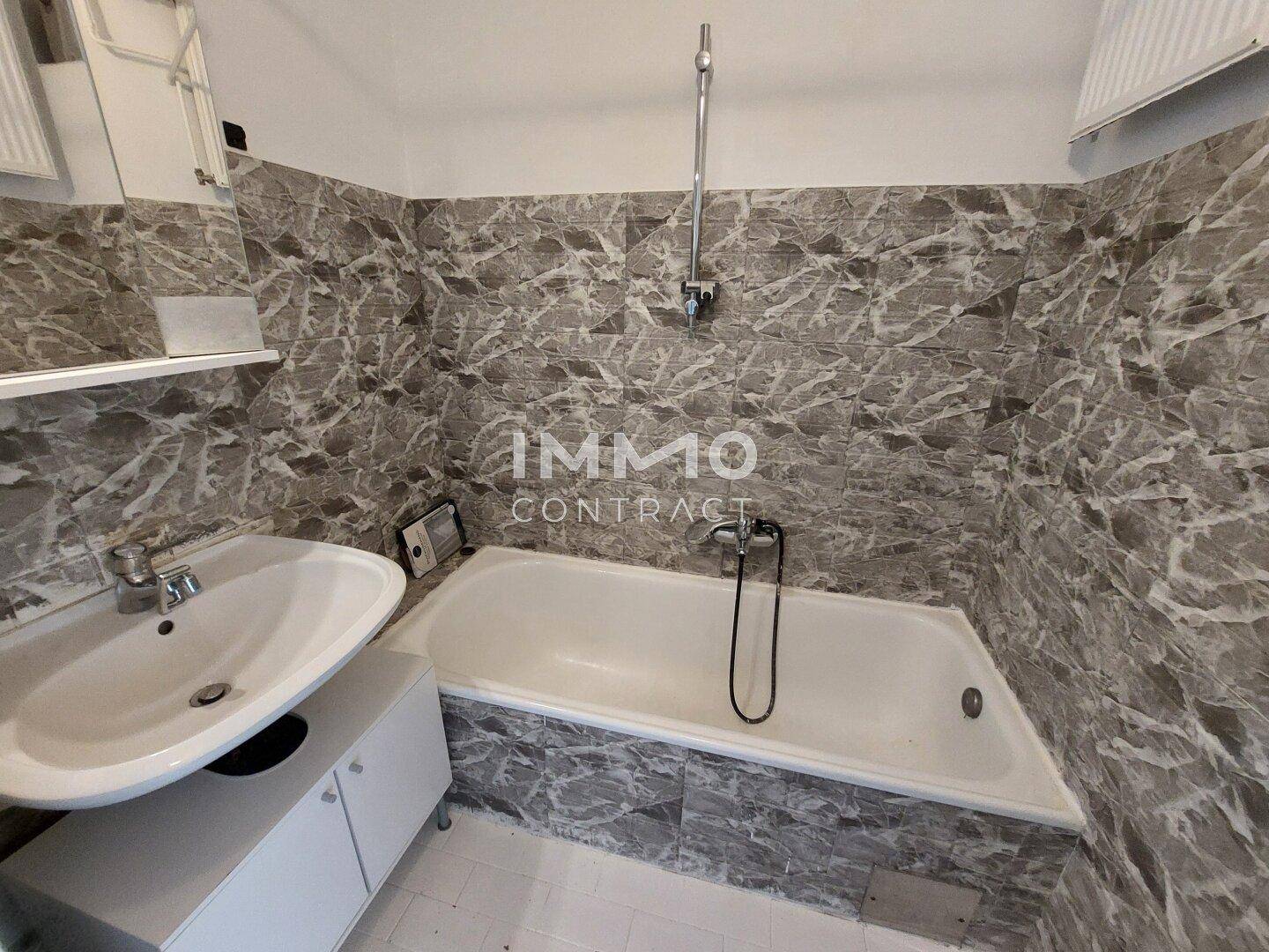 Badezimmer mit Badewanne, Einzelwaschbecken und grauen Fliesen an den Wänden.
