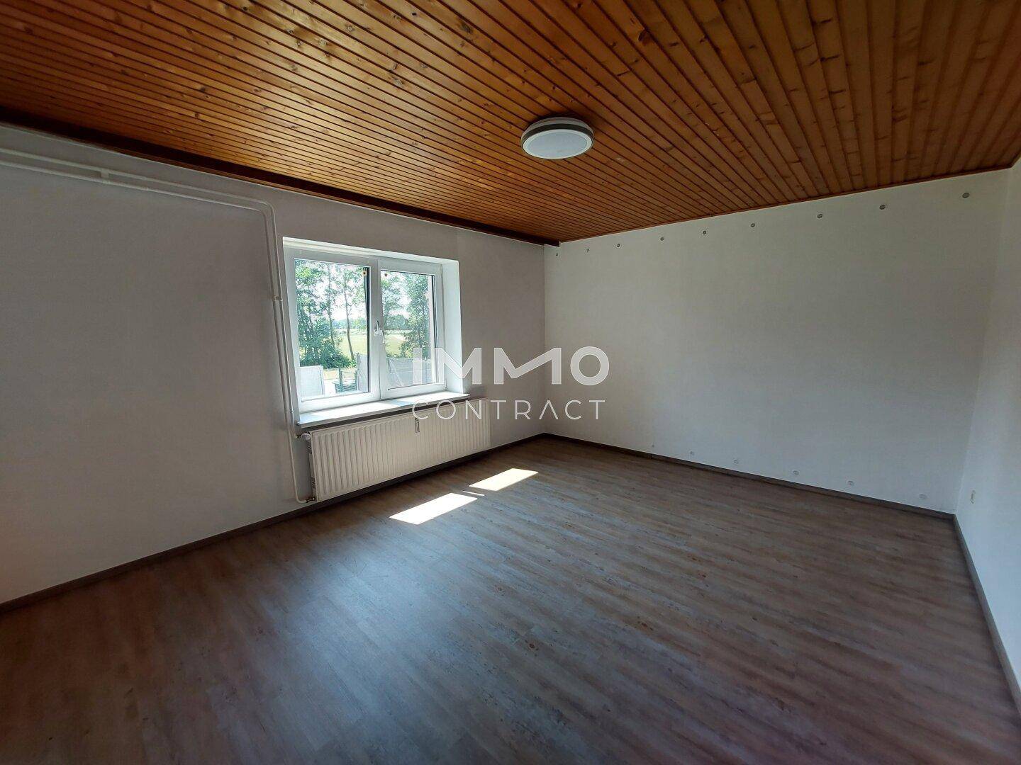 Helles Zimmer mit Laminatboden, Holzdecke und Blick ins Grüne.