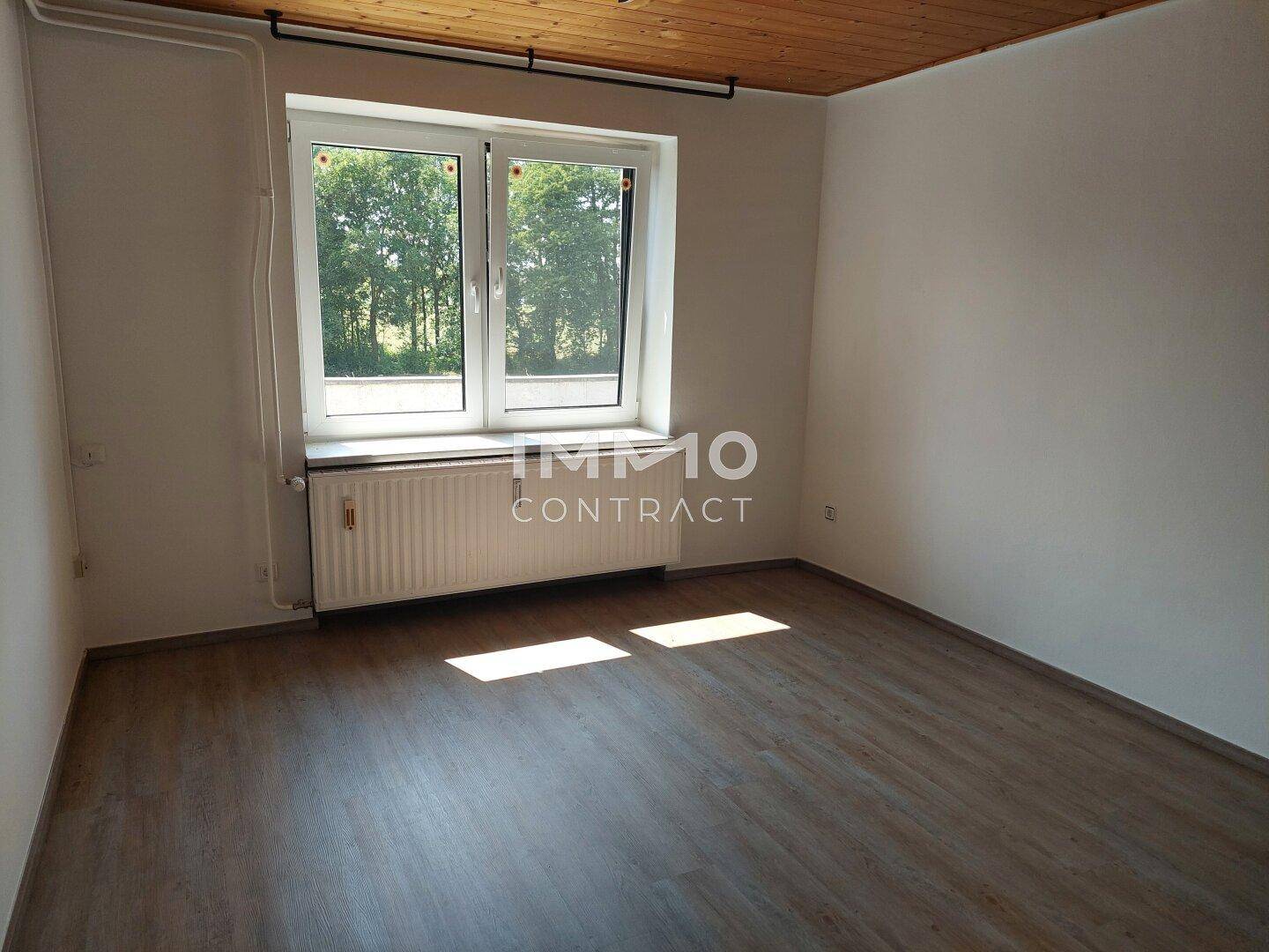 Geräumiges Zimmer mit Laminatboden, Holzdecke und großem Fenster mit Ausblick.