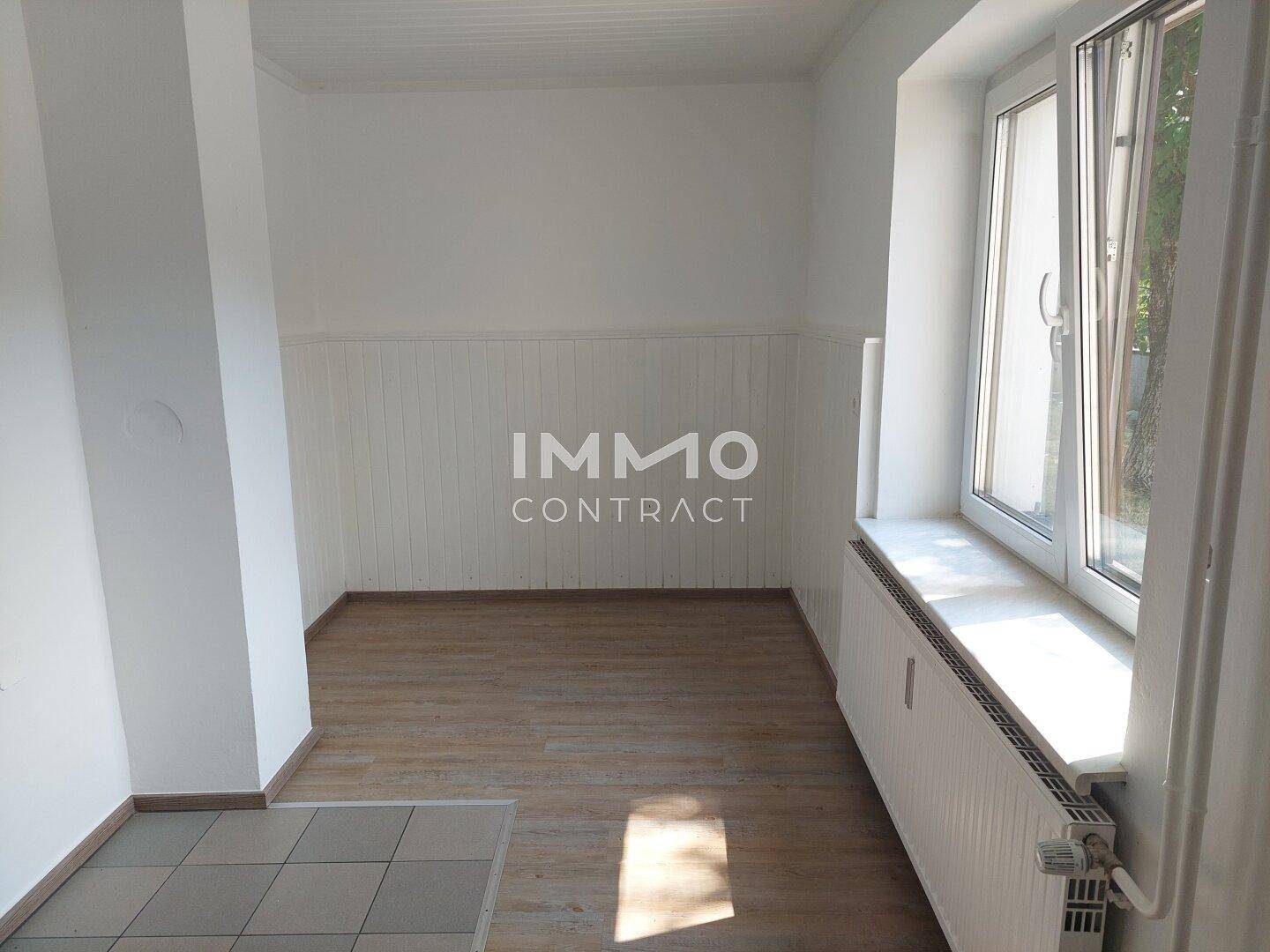 Heller Wohnbereich mit Laminatboden und weißer Holzvertäfelung an der Wand.