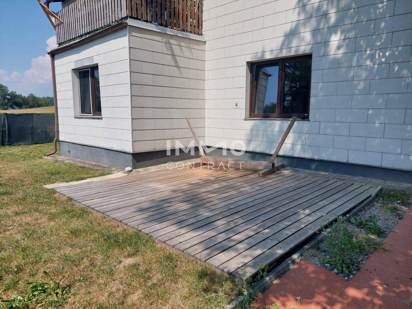 Holzterrasse am Haus, umgeben von Rasen und mit Blick auf die Natur.