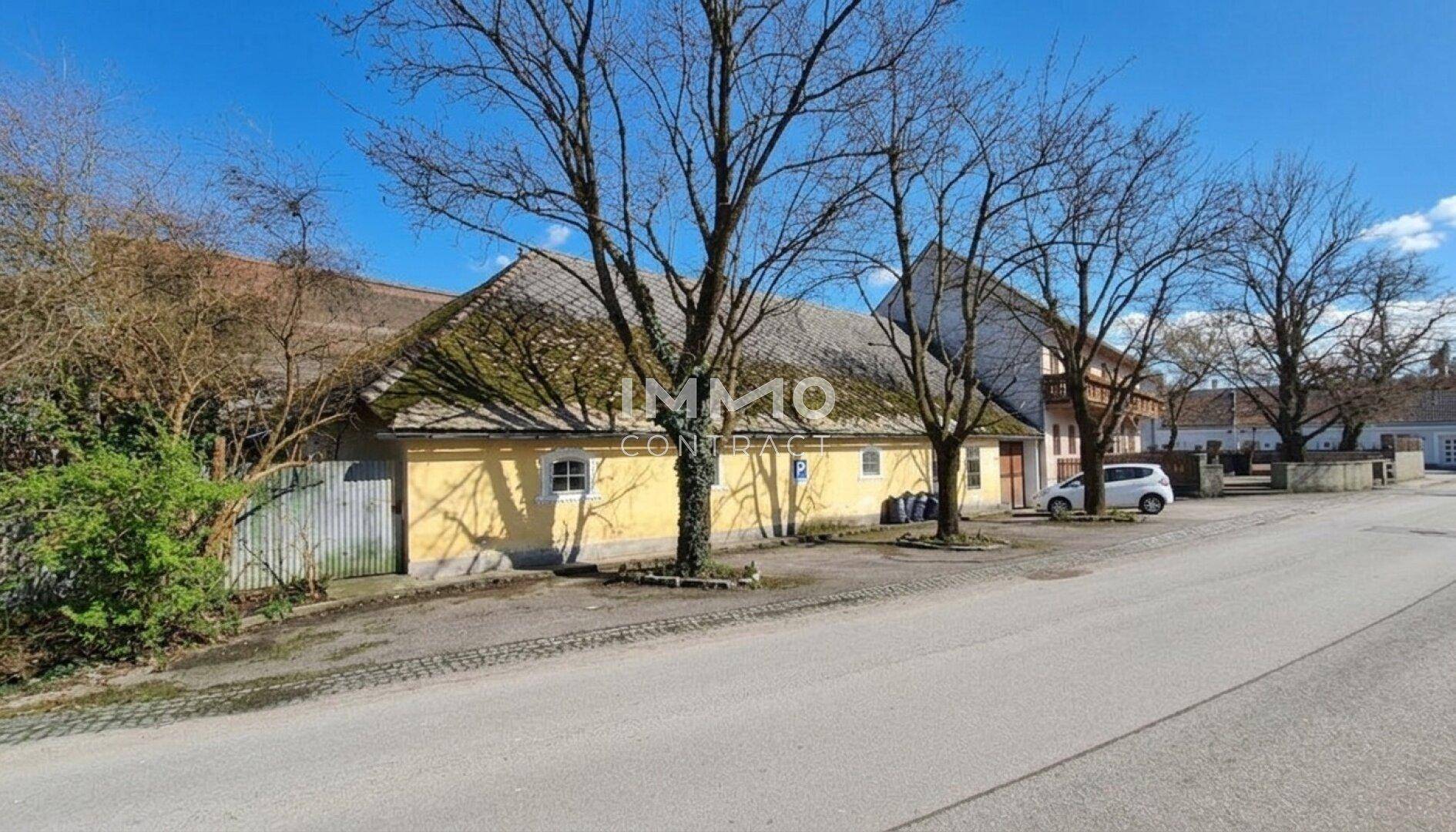 Gelbes Gebäude mit altem Dach und kahlen Bäumen an einer ländlichen Straße.