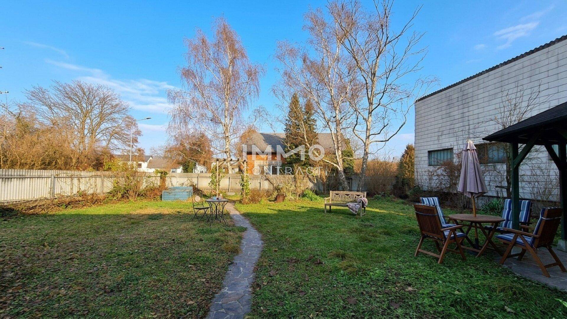 Gepflegter Garten mit Rasenfläche, Bäumen und Sitzgelegenheiten im Freien.