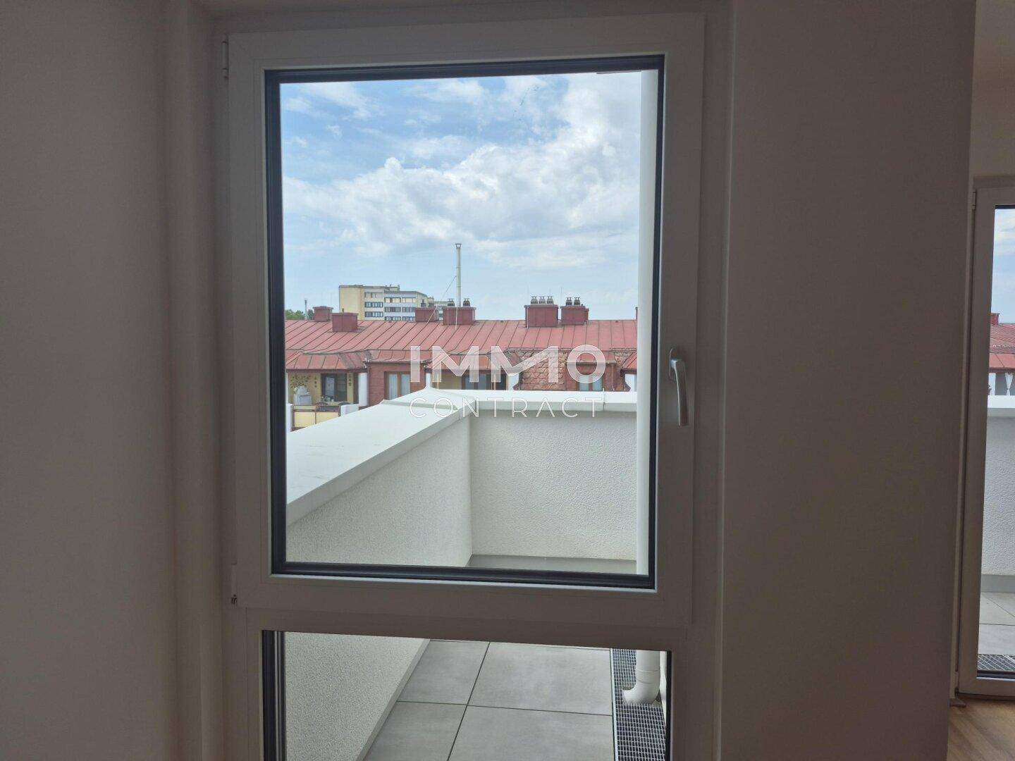 Blick aus dem Fenster auf eine Terrasse und die Dächer der umliegenden Gebäude.