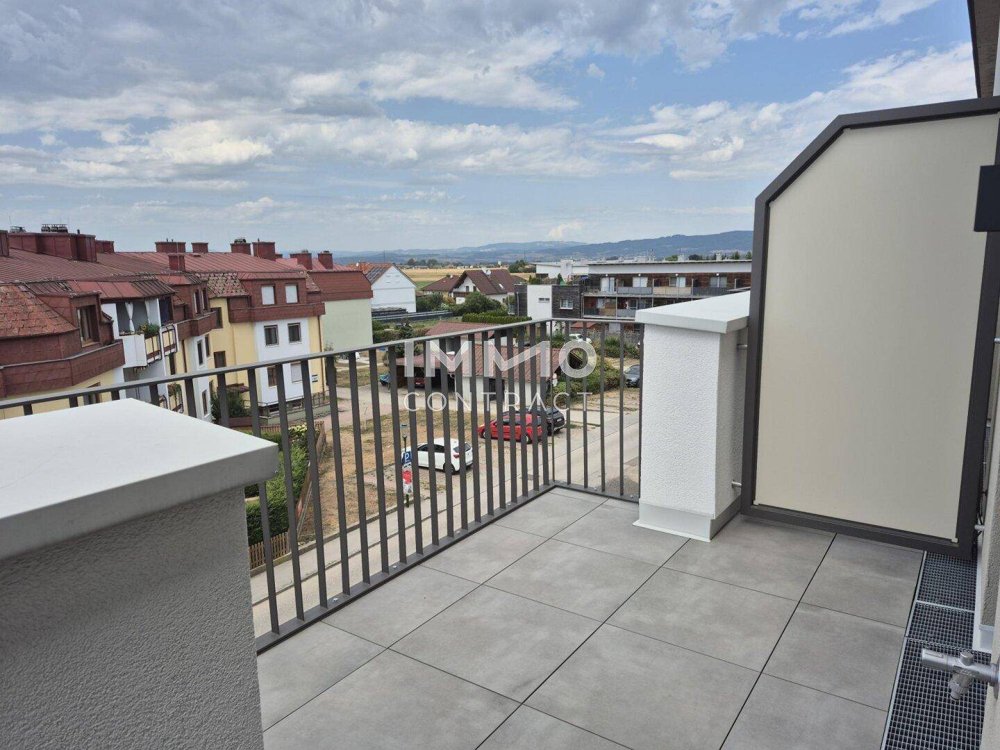 Geräumiger Balkon mit Fliesenboden und Metallgeländer, bietet einen weiten Blick über die Nachbarschaft.