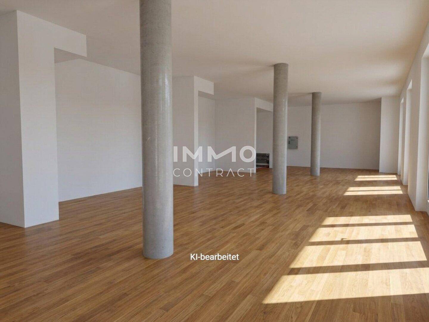 Großer, leerer Gewerberaum mit Holzboden, weißen Wänden und mehreren Betonsäulen, hell beleuchtet durch Tageslicht.