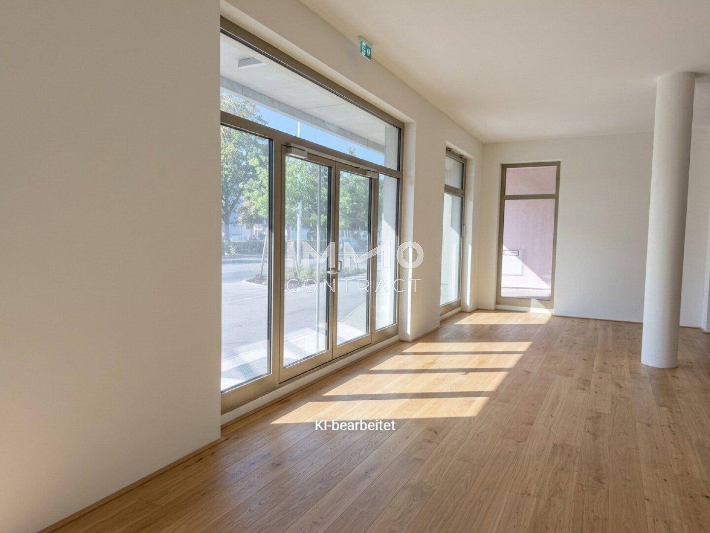 Heller Gewerberaum mit großen Glasfronten, Holzboden und weiß gestrichenen Wänden, bietet viel Tageslicht.