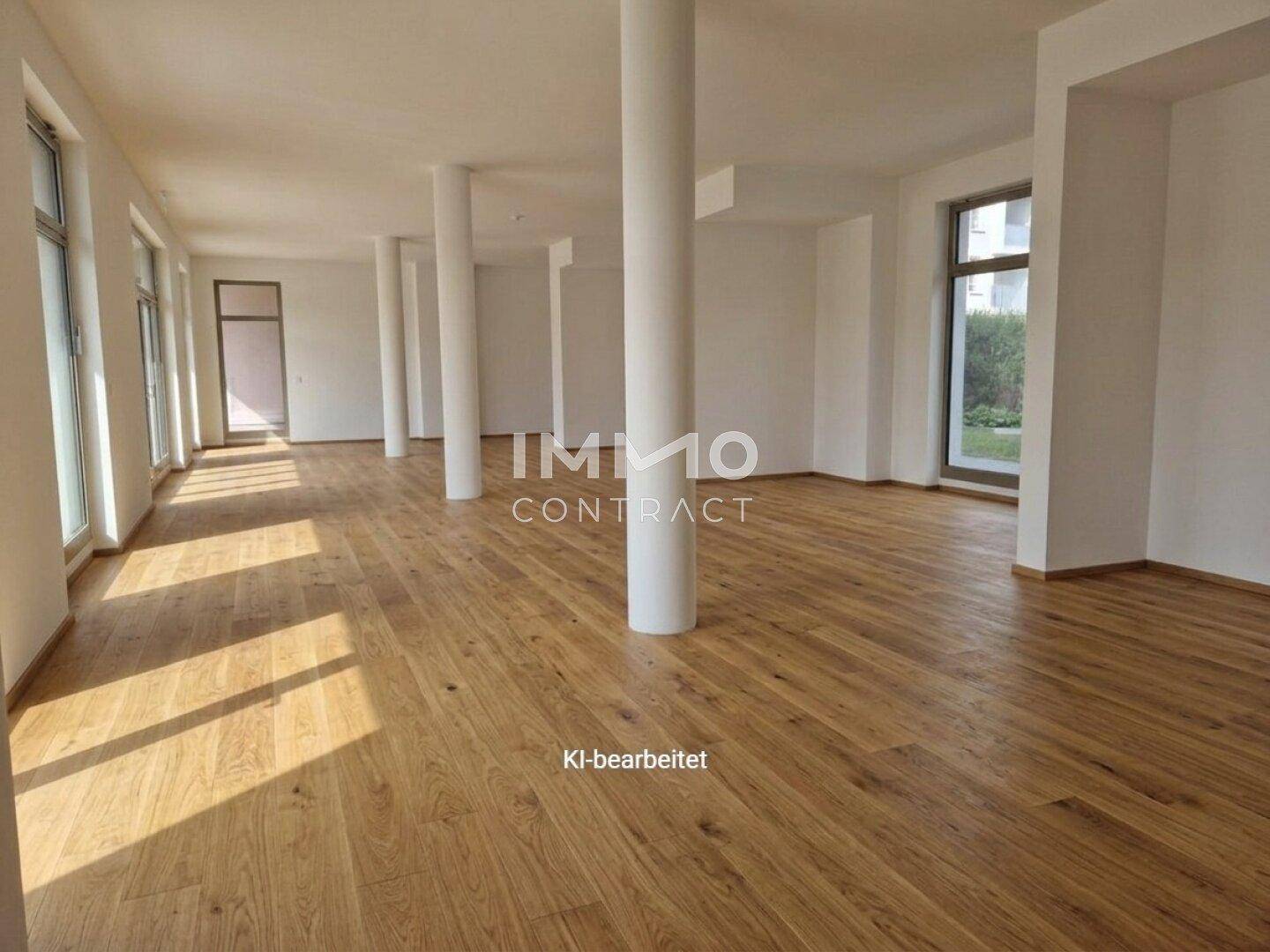 Weitläufiger, leerer Gewerberaum mit Holzboden, weißen Wänden und mehreren tragenden Säulen, gut beleuchtet.