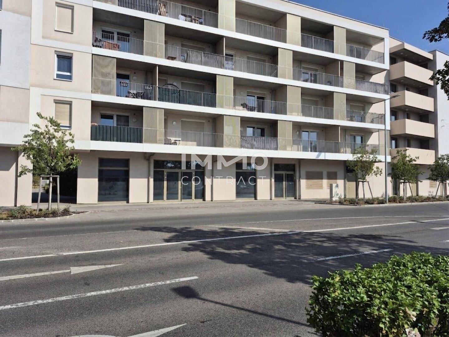 Fassade eines modernen Apartmentgebäudes mit Geschäftsflächen im Erdgeschoss und Balkonen in den oberen Etagen.
