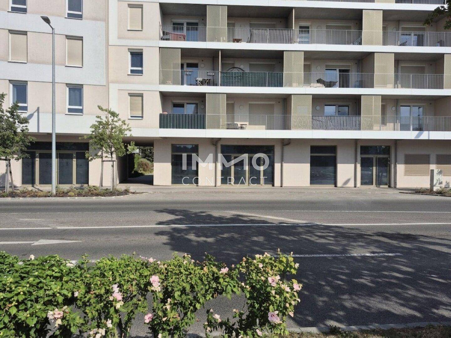Fassade eines modernen Apartmentgebäudes mit Geschäftsflächen im Erdgeschoss und Balkonen, von der Straße aus gesehen.