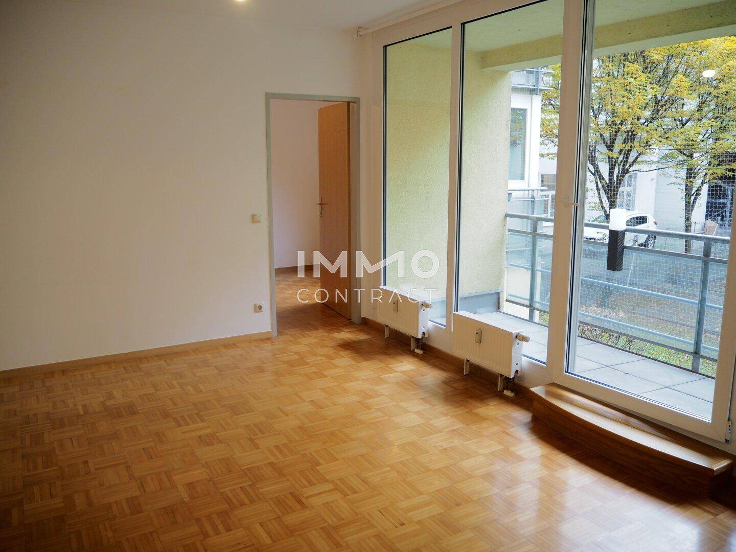 Helles Wohnzimmer mit Parkettboden und breiten Fenstern, die auf einen Balkon führen.