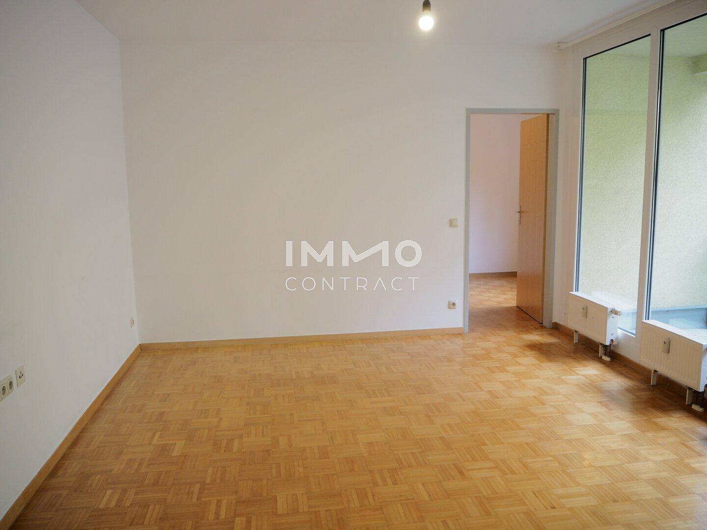Geräumiges Wohnzimmer mit Fischgrätparkett, großen Fenstern und Zugang zum Balkon.